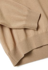 Suéter de cachemira beige con puños y dobladillo acanalados, textura suave y un corte holgado, con costuras visibles y detalles de diseño minimalistas.