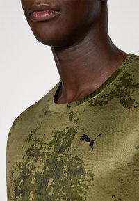 Olijfgroene t-shirt gemaakt van gebreide stof met een zwart Puma-logo. Heeft een ronde hals en een camouflagepatroon met donkere accenten.