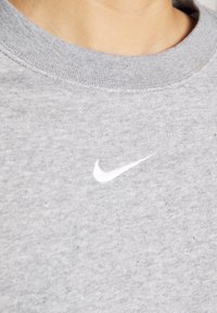 Gros plan d'une personne portant un sweat gris col rond avec un petit logo Nike Swoosh blanc sur la poitrine.