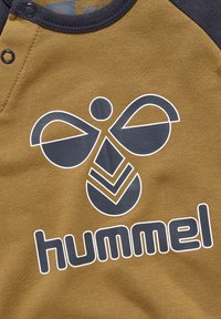 Brun og marineblå kortærmet skjorte med et stort sort grafisk design og ordet "hummel" i fede bogstaver nederst.