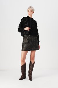 Giacca nera di piume, mini gonna in pelle e stivali da cowboy marroni scuri. Presenta orecchini a cerchio e una piccola borsa a tracolla nera.