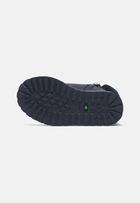 Suela de zapato azul marino con surcos profundos para tracción. Presenta una superficie texturizada y un indicador central en verde. Material de goma duradera.