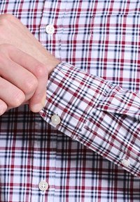 Röd, marinblå och vit rutig skjorta med långa ärmar, med knappstängning och bröstficka. Tyget är slätt, med synliga sömmar.