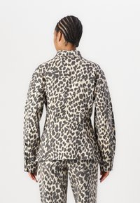 Giacca con stampa leopardo in beige e nero, caratterizzata da un colletto, maniche lunghe e un design su misura. Esibita di spalle con pantaloni abbinati.