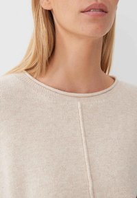 Jasno beżowy sweter z okrągłym dekoltem, z ribbowanym wykończeniem, teksturowanym splotem i centralnym detalem szwu. Miękki i przyjemny w dotyku materiał.