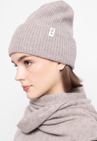 Világosszürke kötött sapka bordás textúrával és hajtott széllel. Kicsi fehér címke fekete betűkkel. Puha anyag.