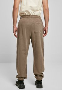 Brune bukser laget av lett stoff, med elastisk midjebånd, løs passform og mansjetterte anklene. Har detaljer med baklomme.