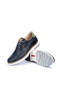 Chaussures en cuir pour hommes avec une tige bleu marine à texture perforée, des accents en cuir vert et une semelle en caoutchouc blanche avec des motifs de semelle en triangle.