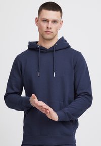 Sudadera azul marino hecha de una tela suave, con un bolsillo tipo canguro, capucha con cordón y puños acanalados, mostrada con una postura erguida.