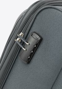 Angolo di una valigia in tessuto grigio con una sicura combinazione nera e zip metalliche; la texture è liscia con una finitura resistente.