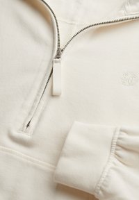 Felpa color crema con zip a quarti, zip in metallo, aletta in tessuto, polsini elastici e logo ricamato discreto sul petto.