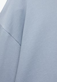 Tissu bleu clair, texturé avec une finition douce. Le matériau semble légèrement extensible, avec un design simple et sans coutures.