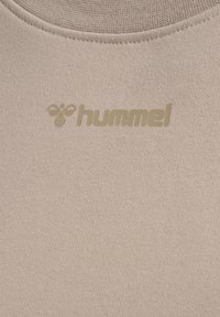 Beige sportstopp i slät, elastisk tyg med rund halsringning och en subtil, präglad logo i guld.