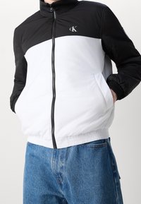 Kurtka bomber Calvin Klein w czerni i bieli, z dwustronnym zamkiem, elastycznymi mankietami oraz kontrastowymi blokami kolorów z detalem logo.