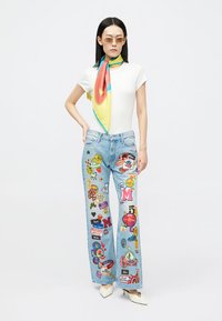 Λευκό κοντομάνικο μπλουζάκι, μπλε τζιν παντελόνι με πολύχρωμες λεπτομέρειες και ένα πολύχρωμο μεταξωτό κασκόλ. Μοντέρνα γυαλιά ηλίου και λευκές μυτερές γόβες.