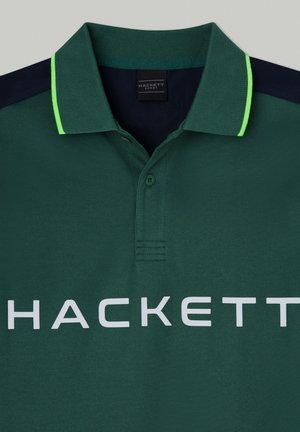 Grön polo skjorta i strukturerad tyg, med en marinblå krage med neongröna detaljer och en stor vit "HACKETT"-logotyp på framsidan.