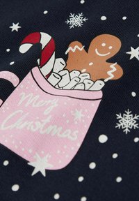 Różowa filiżanka z piankami, pierniczkowym ludkiem i cukierkiem w czerwono-białe paski, na tle ciemnego tła z białymi płatkami śniegu i gwiazdami.