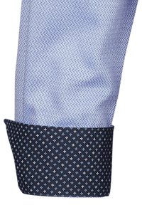 Tessuto della camicia di colore azzurro chiaro con un motivo testurizzato, caratterizzato da un polsino blu navy decorato con un piccolo motivo di diamanti azzurri chiari e bianchi.