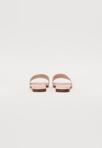 Růžové ploché sandály s minimalistickým designem, které mají dva široké popruhy a plochou hnědou podrážku. Hladký povrch bez viditelného kovového materiálu.