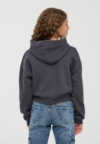 Ciemnoszary hoodie o luźnym kroju, z dużym kapturem i prążkowanymi mankietami. W połączeniu z jasnoniebieskimi dżinsami. Teksturowana tkanina.