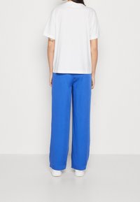 Bílá bavlněná trička s krátkým rukávem v kombinaci s modrými lněnými kalhotami s širokým střihem. Oblečení se vyznačuje volným střihem a minimalistickým designem.