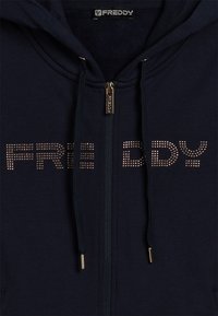 Felpa blu navy con zip frontale, pull della zip dorato, lacci con punte dorate e "FREDDY" in borchie dorate sul petto.