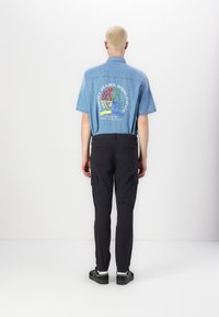 Denim skjortor med kort ärm i ljusblått med en färgglad grafisk design på ryggen. Svarta cargobyxor med sidofickor och en åtsittande stil.