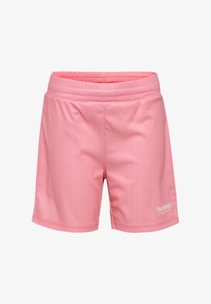 Młoda dziewczyna o rudych włosach w różowym stroju sportowym stoi z rozstawionymi nogami na białym tle.