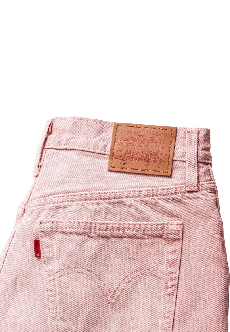Jeans en denim rose clair avec une étiquette en cuir sur la taille. Les caractéristiques incluent des poches arrière avec un design brodé et un onglet logo rouge.