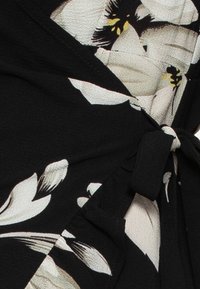 Černé květinové zavinovací šaty s bílými a žlutými květinovými vzory, lehká tkanina, detail vázání v pase a texturovaný povrch.