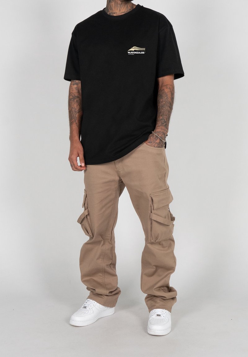 Svart bomulls-T-shirt med liten logga på bröstet, kombinerad med lösa beige cargobyxor med flera sidofickor och vita sneakers.