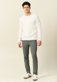 Witte kabelgebreide trui met structuurpatroon, grijze op maat gemaakte broek en witte sneakers met groene strepen en beige accenten.