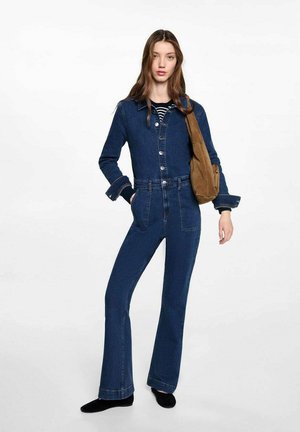 Denim jacket with buttons, paired with high-waisted flared jeans in a dark blue shade. Model carries a brown bag, wearing black footwear.