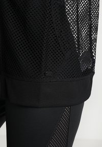 Close-up of black breathable mesh sportswear with solid fabric hem and leggings featuring mesh panel detail.