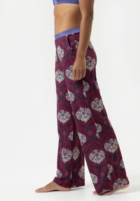 Bloemenpatroon, brede broekspijpen in een diepe kastanjebruine kleur, gemaakt van zacht materiaal. Kenmerkt zich door een blauwe tailleband en ingewikkelde witte en groene ontwerpen.