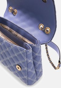 Liliowa torebka ze sztucznej skóry z pikowanym wzorem, białym przeszyciem, złotymi elementami i łańcuszkowym paskiem. Wnętrze posiada dwie przegrody.