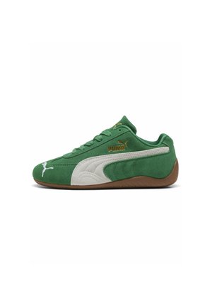 Zapatilla Puma de ante verde con franja blanca, logo dorado de Puma y suela marrón, mostrada en perfil lateral sobre fondo blanco.