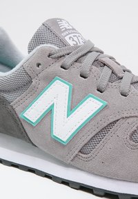 Baskets New Balance 373 grises avec tige en suède et mesh, logo "N" blanc et turquoise, lacets gris.