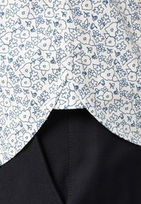 Materiał w kwiaty z niebieskimi konturami na białym tle, cechujący się zaokrąglonym dołem i kontrastującym czarnym materiałem poniżej.