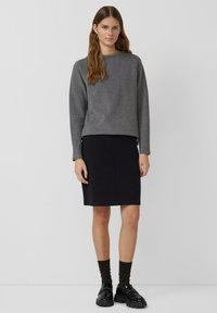 Grijze trui, donkere kokerrok, donkere sokken en glanzende zwarte schoenen. Zachte textuur, minimalistisch ontwerp en eenvoudige lijnen overal.