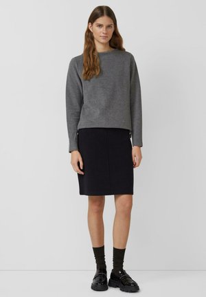 Felpa grigia, gonna a tubino scura, calzini scuri e scarpe nere lucide. Tessuto morbido, design minimale e linee semplici in tutto.