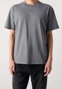 Grijze katoenen T-shirt met een ronde hals en korte mouwen. Heeft een vage logo op de borst. Gecombineerd met donkere jeans voor een casual look.