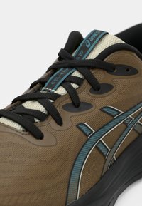 Zapatilla de running marrón con cordones negros, parte superior texturizada, acentos azules y un diseño de suela acolchada. Presenta una lengüeta de textil transpirable.
