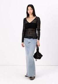 Top lungo a maniche con pizzo nero e scollo a V, abbinato a una lunga gonna in denim blu chiaro. Tiene una borsa a tracolla nera con motivo, indossando scarpe con stampa animale.