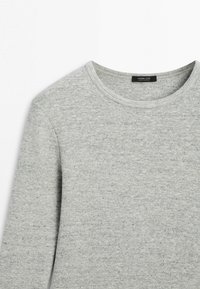 Hellgrauer Pullover mit Rundhalsausschnitt, weicher Stricktextur und langen Ärmeln, Vorderseite oben und Etikett innen am Kragen sichtbar.