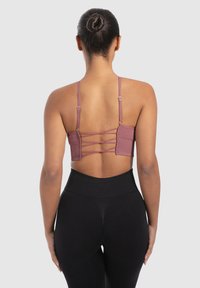 Geribbelde, mauve bralette met verstelbare banden en kruislingse details op de rug. Gecombineerd met hoge zwarte leggings.