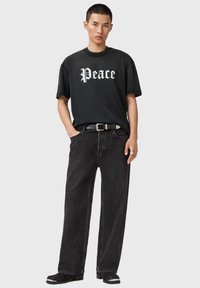 Fekete pamut póló fehér "Peace" felirattal, laza szabású fekete farmernadrággal és ezüst díszítésű fekete övvel párosítva.