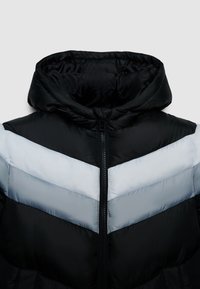 Veste matelassée avec une capuche noire et une fermeture éclair à l'avant. Présente un motif en chevrons dans des nuances de noir et gris clair sur la poitrine.