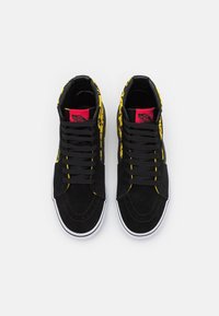 Černé vysoké tenisky se žlutým graffiti potiskem, z materiálu semiš, bílé gumové podešve a černými tkaničkami s červeným logem na jazyku.