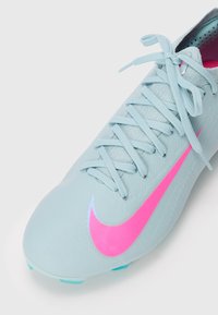 Jasnoniebieskie korki do piłki nożnej z różowym logo Nike, wyściełanym językiem, związanymi sznurówkami i turkusowymi wkrętami na białym tle.